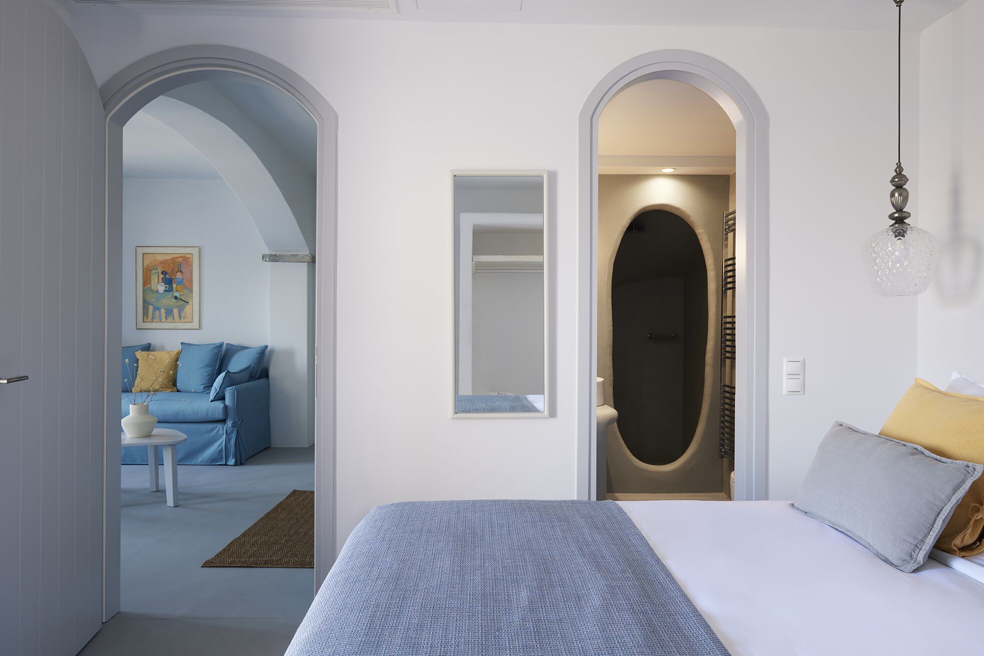 A bedroom with a bed, a bedside table, a mirror, and an arched doorway leading to a bathroom.
