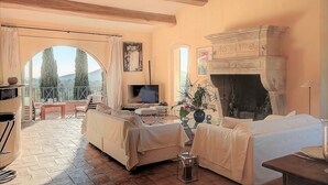 A cozy living room with a fireplace, a TV, and a balcony with a view of the countryside. - St Tropez, large park, unbelievable view sea-forests-hills, 8 bedroom, pool 65ft (Ramatuelle)