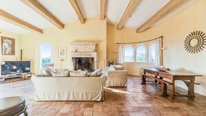 A living room with a fireplace, a sofa, a table, and a TV. - St Tropez, large park, unbelievable view sea-forests-hills, 8 bedroom, pool 65ft (Ramatuelle)