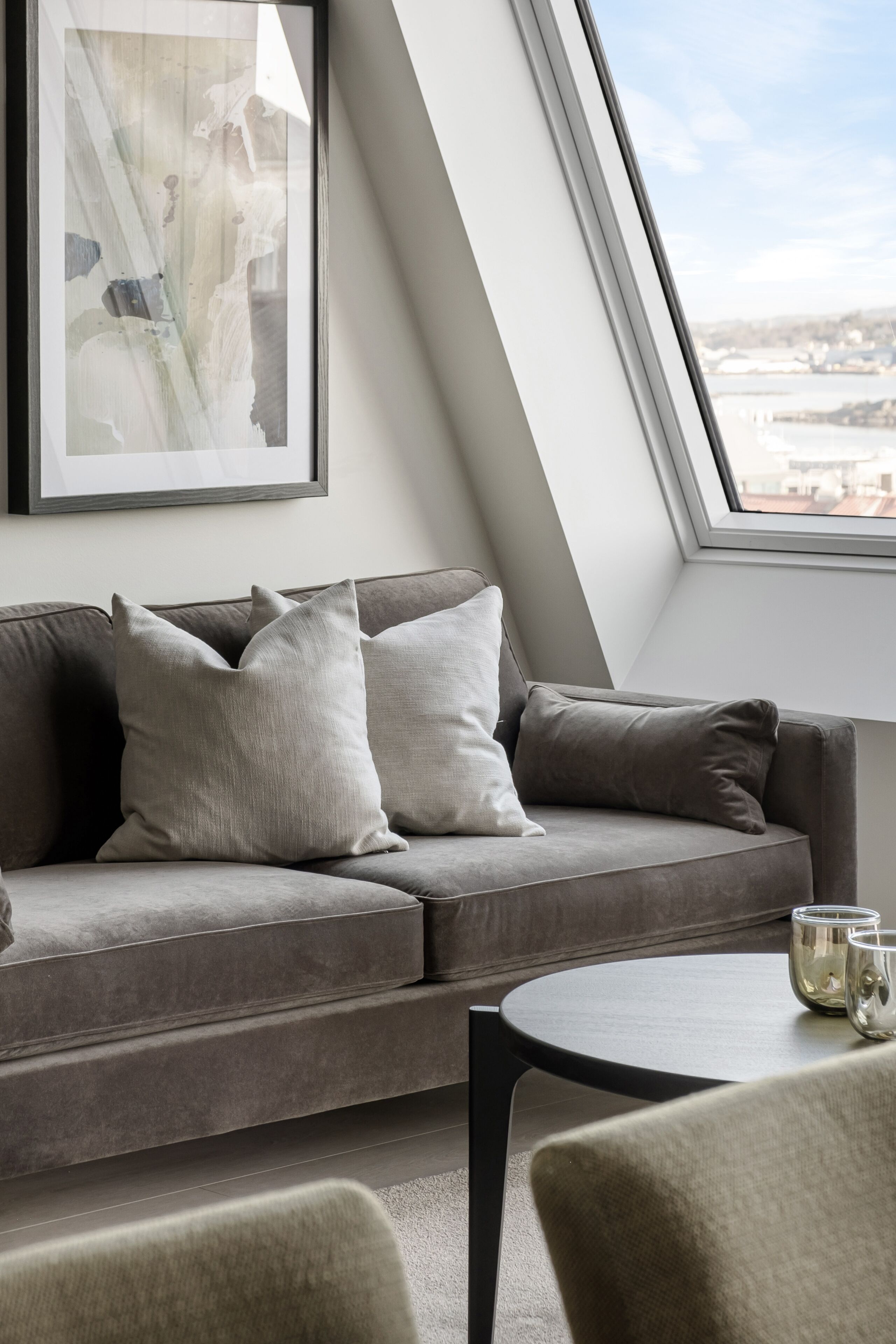 Ein modernes Wohnzimmer mit einem grauen Sofa, zwei Kissen, einem kleinen runden Tisch und einem gerahmten abstrakten Kunstwerk an der Wand.