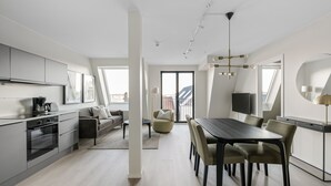 A modern apartment with a kitchen, dining area, and living space. It features a large window, a dining table with chairs, a sofa, and a TV. - VANDER - Pedersgata (Stavanger)
