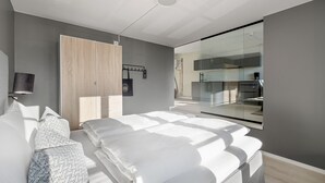 A modern bedroom with a large bed, a wardrobe, a mirror, and a view of the kitchen through a glass partition. - VANDER - Pedersgata (Stavanger)