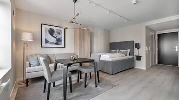 A modern hotel room with a sofa, a dining table, a bed, and a large window.