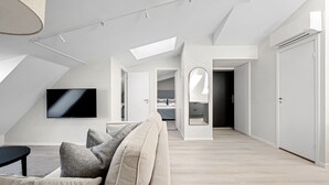 A modern loft apartment with a high ceiling, skylight, a flat-screen TV, a sofa with patterned cushions, and a minimalist design. - VANDER - Pedersgata (Stavanger)