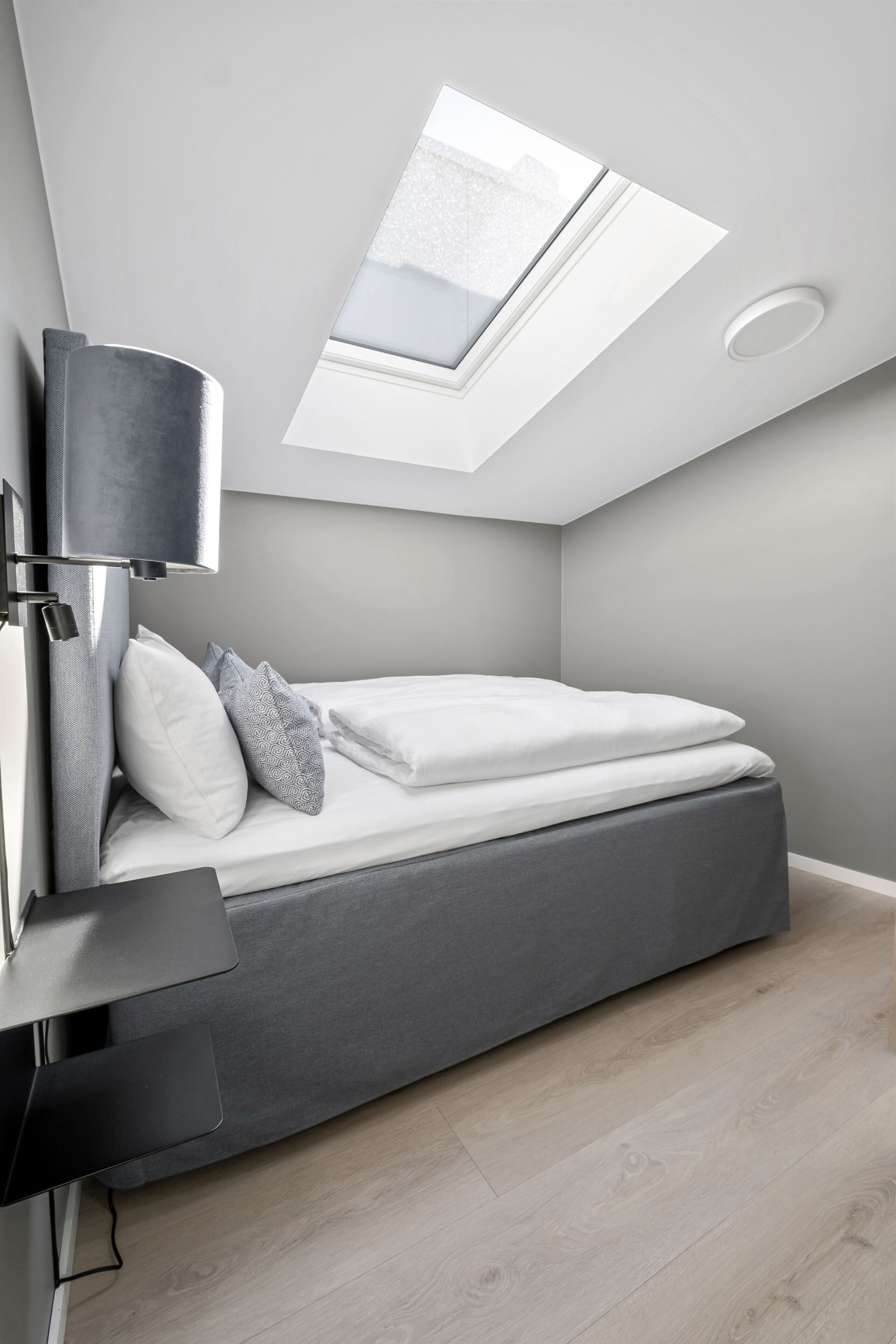 A modern bedroom with a skylight, a bed with white bedding, and a grey headboard.