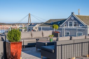A deck with outdoor furniture, a potted plant, and a view of a bridge and buildings in the background. - VANDER - Pedersgata (Stavanger)