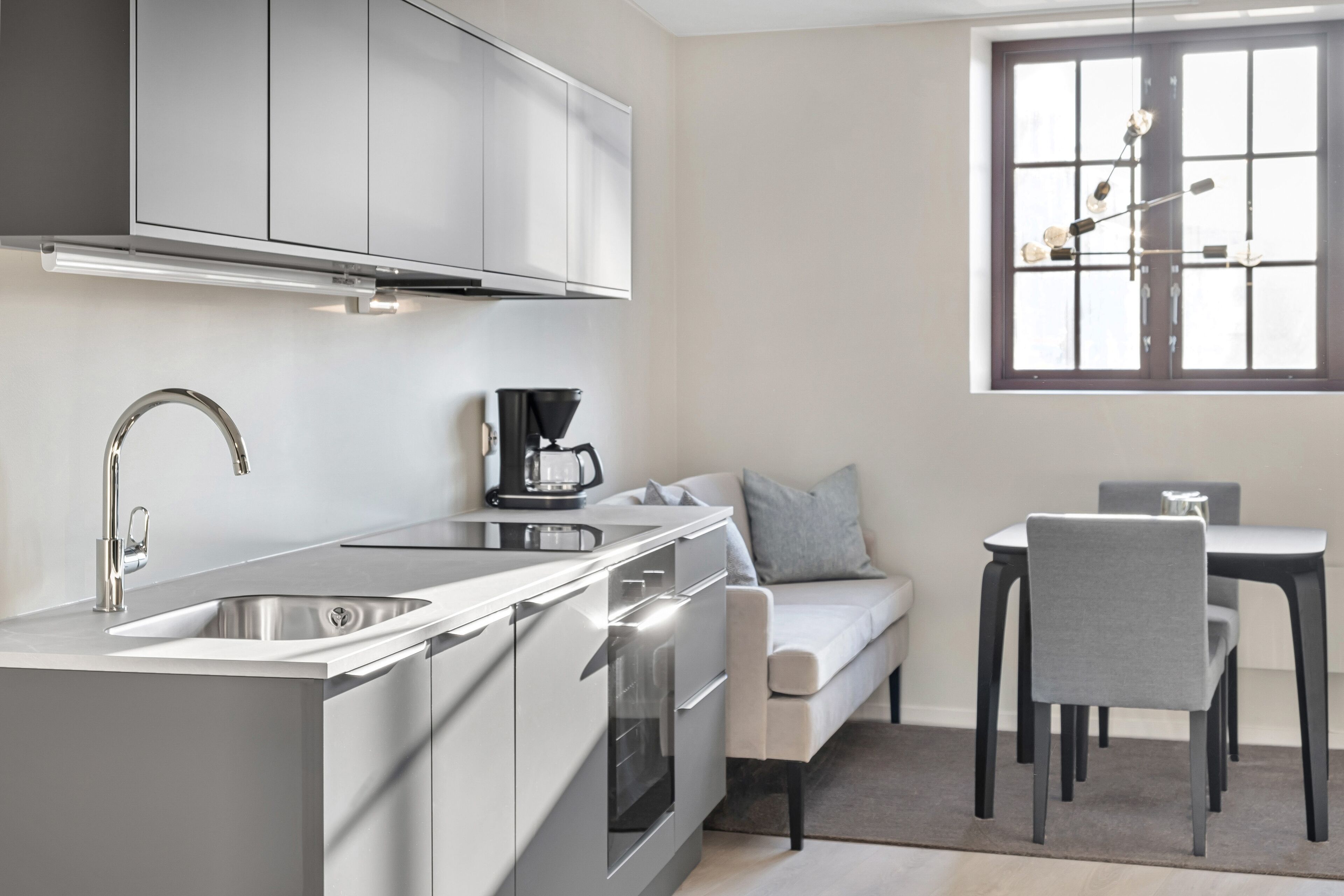 A modern kitchen with stainless steel appliances, a built-in oven, and a coffee maker. There is a dining area with a table and chairs, and a window with a view of the outside.