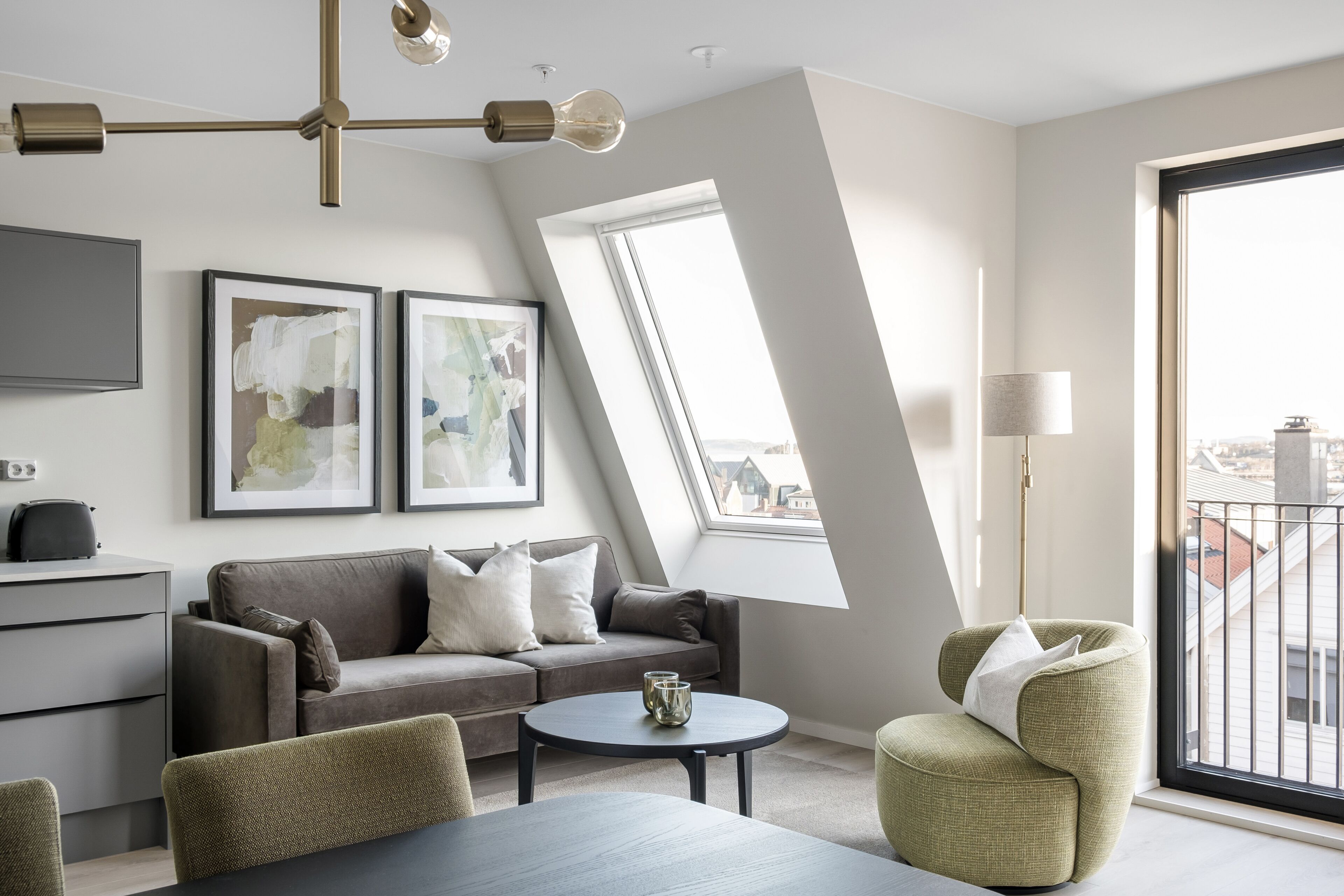 A modern living room with a sofa, a coffee table, and a chair. There is a TV on the wall and a window with a view of buildings.