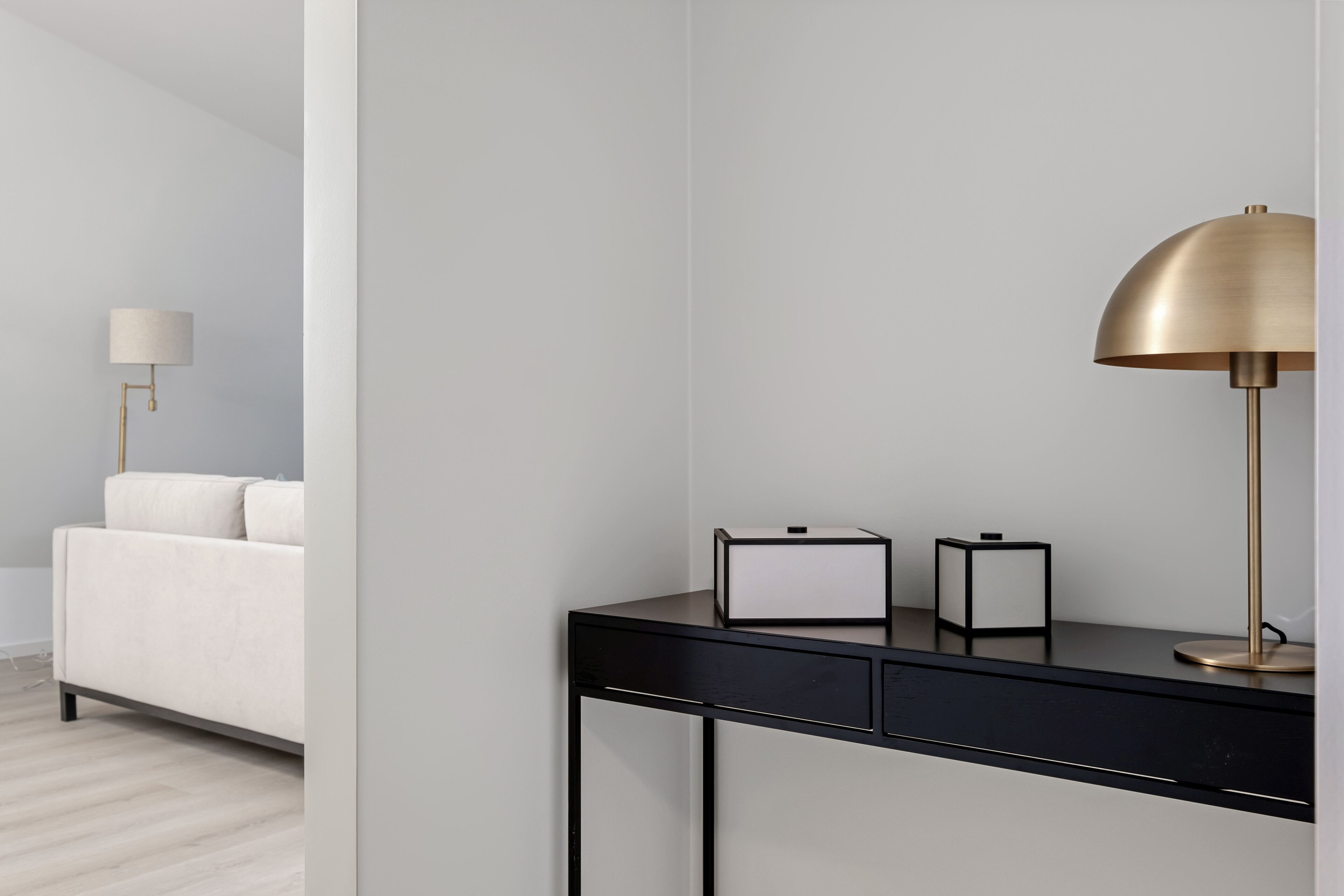 A modern, minimalist room with a black desk, a gold lamp, and a white sofa.