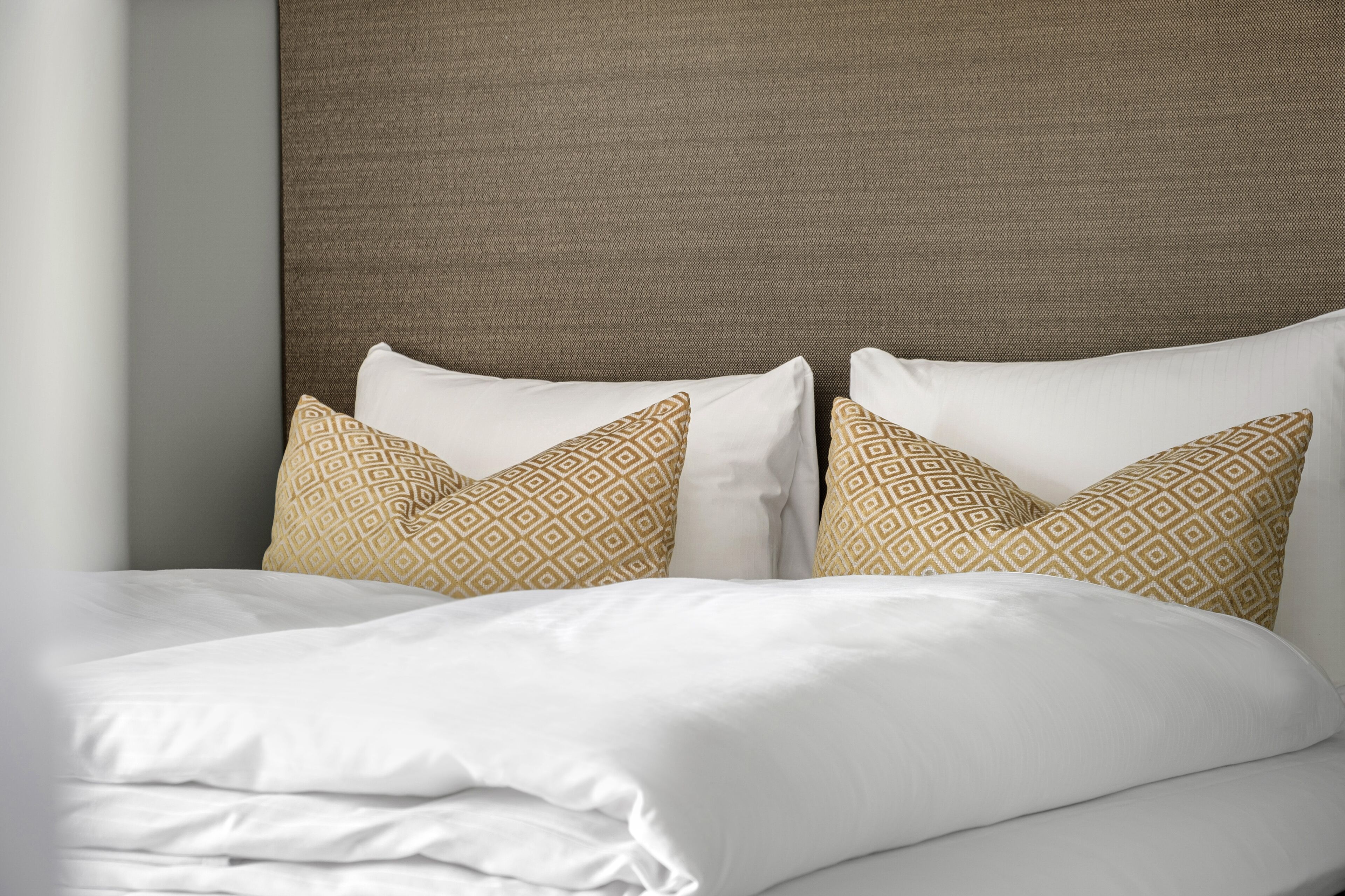 A neatly made bed with white linens and patterned pillows.