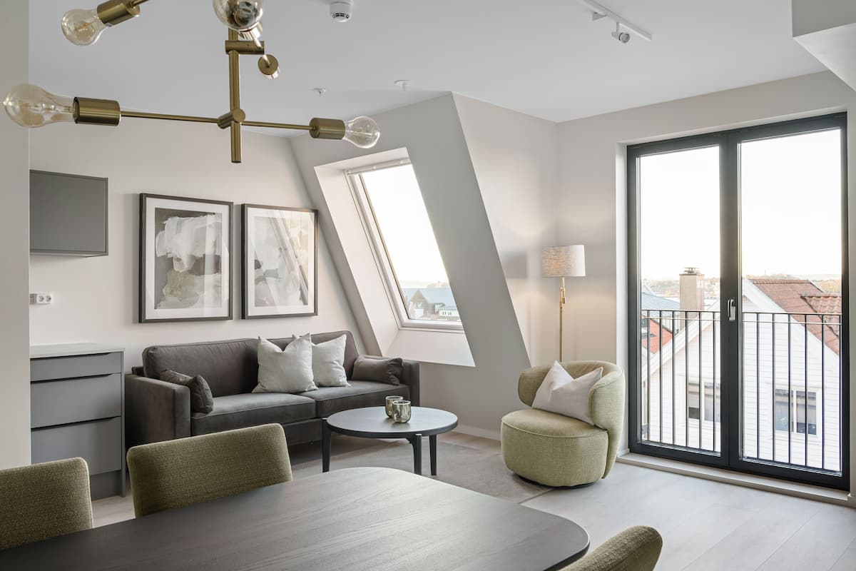A modern living room with a sofa, a dining table, and a balcony with a view.
