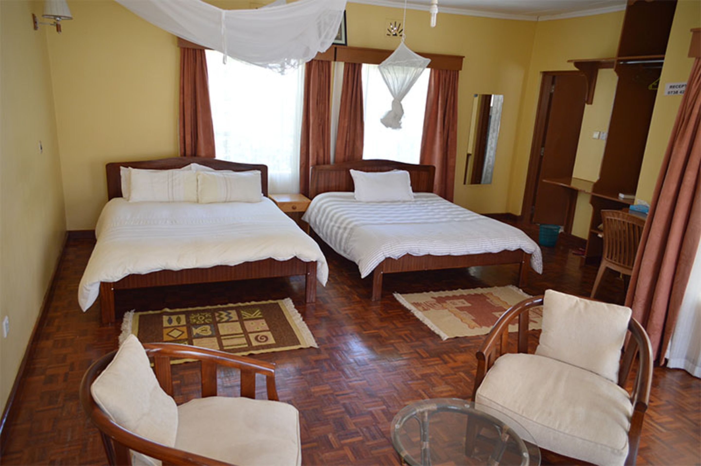 A hotel room with two beds, a sitting area with chairs, a small table, and a wooden floor.