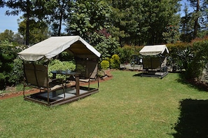 Two outdoor seating areas with tables and chairs under canopies, surrounded by well-maintained grass and various shrubs. - Gracemont Guesthouse (Eldoret)