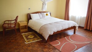 Ein Schlafzimmer mit einem hölzernen Bett, einem Nachttisch, einem Sessel, einem gemusterten Teppich und einem Fenster mit Vorhängen.