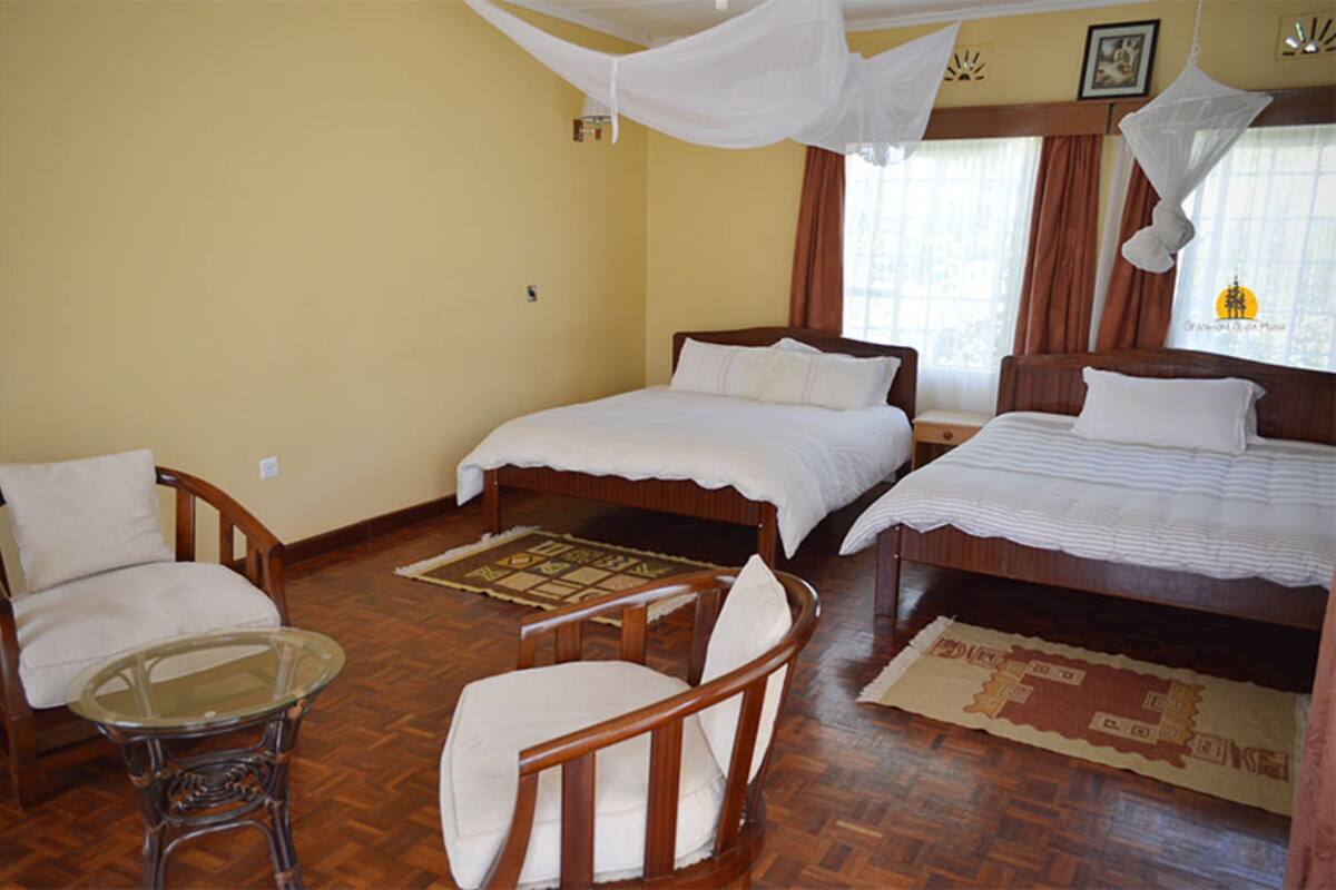 Quarto de hotel com duas camas, uma cadeira de madeira, uma mesa de vidro e piso de madeira.