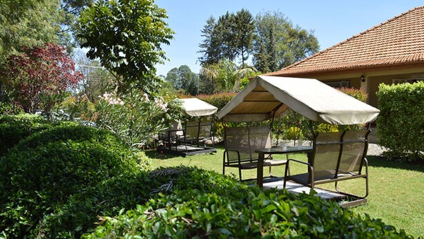 Ein Garten mit überdachter Sitzgelegenheit, einem Gebäude mit Ziegeldach und üppiger Bepflanzung.