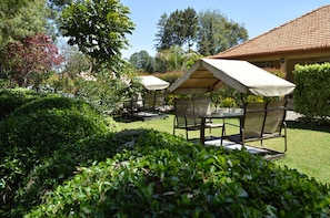A garden area with a covered seating area, a building with a tiled roof, and lush greenery. - Gracemont Guesthouse (Eldoret)