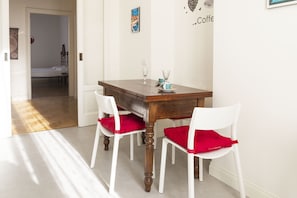 Un coin repas avec une table en bois, des chaises blanches dotées de coussins rouges et une décoration murale sur le thème du café.