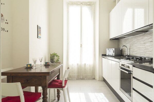 Una cocina con armarios blancos, una mesa de madera y una silla roja.