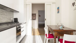 A modern kitchen with a black countertop, stainless steel appliances, and a wooden dining table with red cushions.