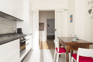 Una cocina moderna con encimera negra, electrodomésticos de acero inoxidable y una mesa de comedor de madera con cojines rojos.