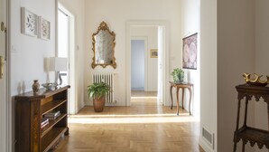A hallway with a wooden floor, a radiator, a mirror, and a door leading to another room.