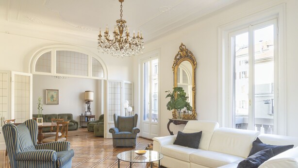 A spacious living room with a white sofa, striped armchairs, a round coffee table, and a chandelier.