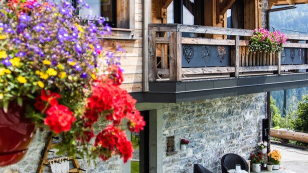 A wooden chalet with a balcony, stone walls, wicker furniture, and a hanging flower basket. - Les Gets, Luxury duplex apartment with Jacuzzi (Les Gets)