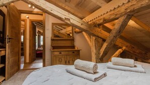 A bedroom with a high ceiling and exposed wooden beams, a bed with white linens, and a wooden dresser. - Les Gets, Luxury duplex apartment with Jacuzzi (Les Gets)