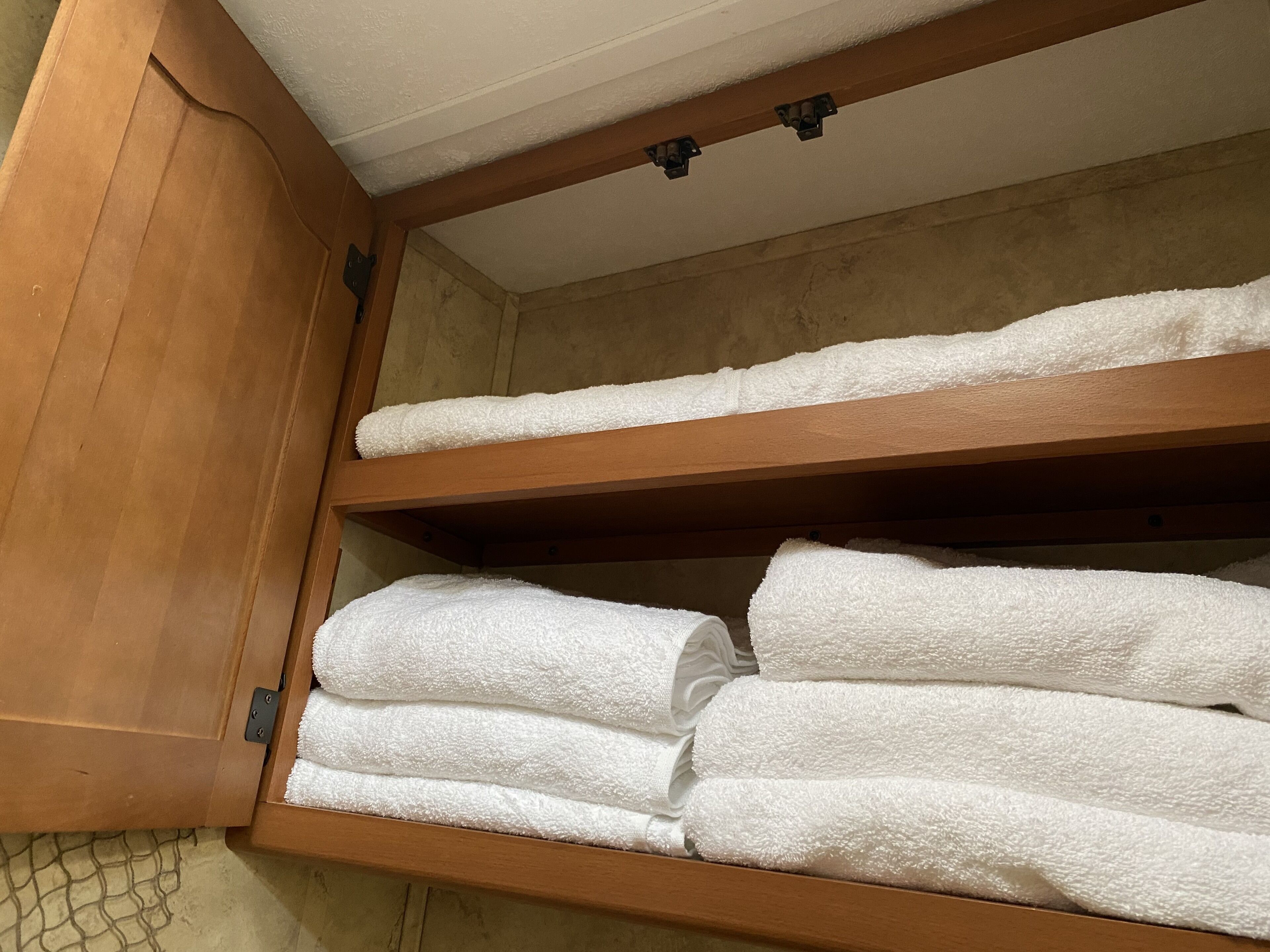 A wooden cabinet with three shelves holding white towels.