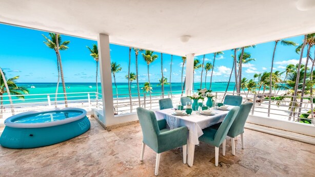 Un área de comedor con vistas a la playa y al océano, una bañera de hidromasaje redonda y una mesa lista para cuatro personas.