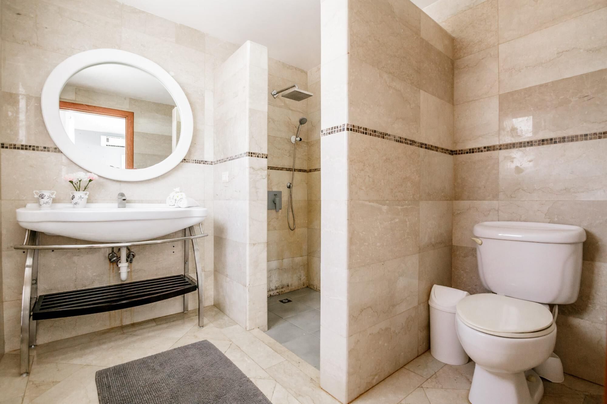 Une salle de bain équipée d’un lavabo, d’un miroir, de toilettes, d’une douche et d’un petit tapis sur le sol.