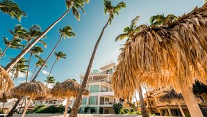 Un hotel frente a la playa con palmeras, una playa de arena y un edificio de varios pisos con balcones.