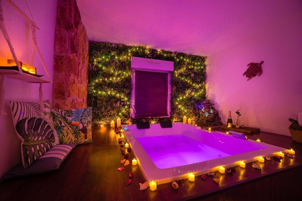 A room with a large bed, a wall-mounted air conditioner, a small table with a bottle and glass, and a decorative wall with plants and lights.
