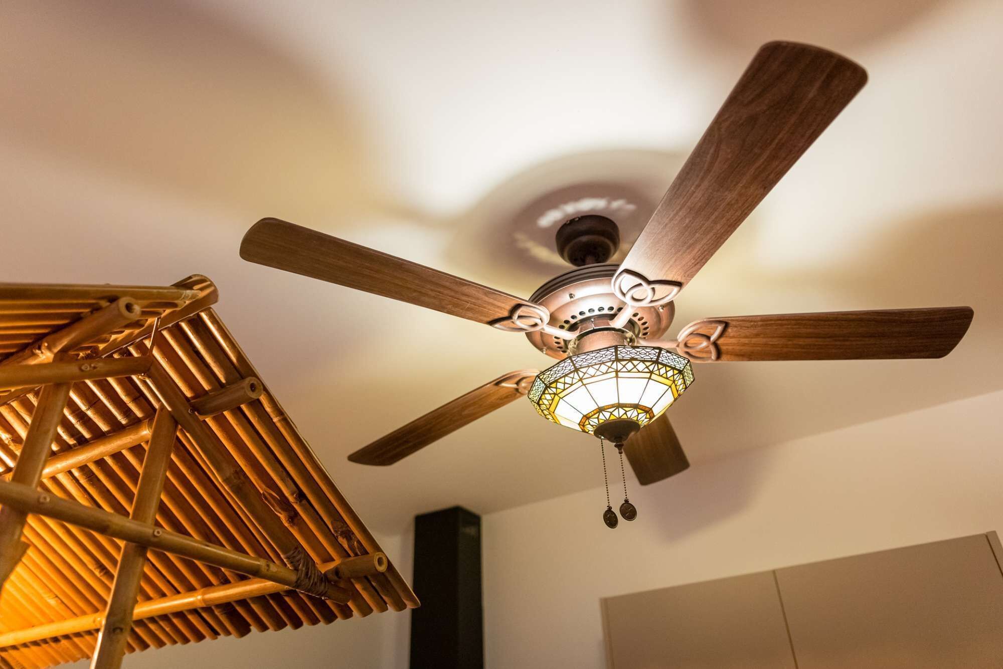 Ein Deckenventilator mit Holzflügeln und einer dekorativen Lampenleuchte.