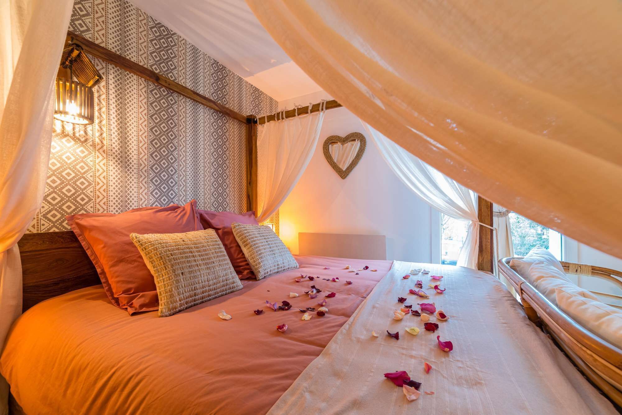 A bedroom with a canopy bed, patterned wallpaper, a heart-shaped decoration on the wall, and a bedside lamp.