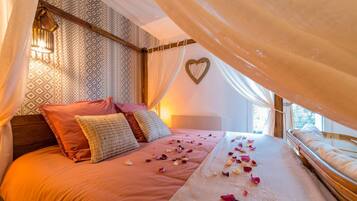A bedroom with a canopy bed, patterned wallpaper, a heart-shaped decoration on the wall, and a bedside lamp.