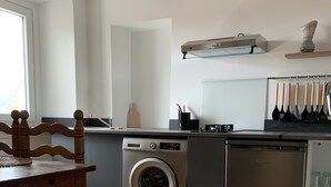 Une cuisine moderne équipée d’un lave-linge et d’un sèche-linge intégrés, d’une table à manger en bois et d’une fenêtre laissant entrer la lumière naturelle.