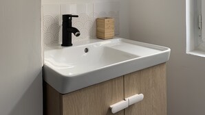 Une salle de bain avec un lavabo blanc, un robinet noir et un miroir rond.
