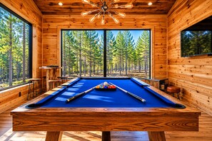 Una mesa de billar en una sala de madera con ventanas amplias y vistas a un bosque.