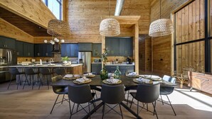 A modern kitchen with wooden walls, a central island, and a dining area with a large table and chairs. - Sunlit Spaces • 6-Bunk Room • Big Porch Fun (Broken Bow)