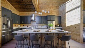 A modern kitchen with dark cabinets, stainless steel appliances, and a central island with bar stools. - Sunlit Spaces • 6-Bunk Room • Big Porch Fun (Broken Bow)