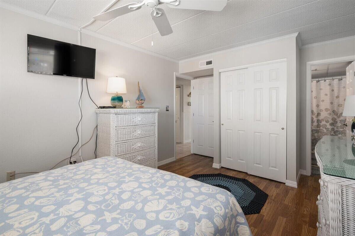 A bedroom with a bed, a ceiling fan, a TV, a dresser, and a door leading to another room.