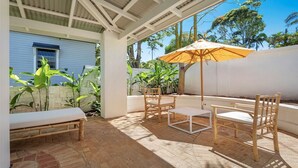 A covered outdoor seating area with a table and chairs, a bench, and an umbrella. - Le Dog Beach Club - chic home with pool (Byron Bay)