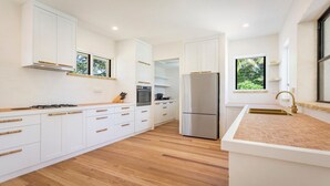 A modern kitchen with white cabinetry, a stainless steel refrigerator, and a wooden countertop. - Le Dog Beach Club - chic home with pool (Byron Bay)