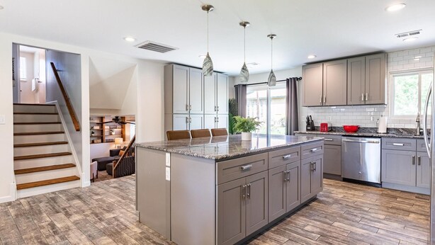 A modern kitchen with grey cabinets, a central island, and a wooden staircase. - Cozy, Clean and Bright 4BR / 2BA Home! Welcome! (Sterling Heights)