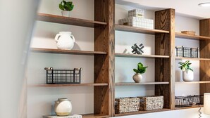 A wall with wooden shelves displaying various decorative items and storage baskets. - Cozy, Clean and Bright 4BR / 2BA Home! Welcome! (Sterling Heights)