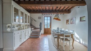 Un'ampia cucina con mobili bianchi, una scala in legno e un'area pranzo con tavolo imbandito per quattro persone.