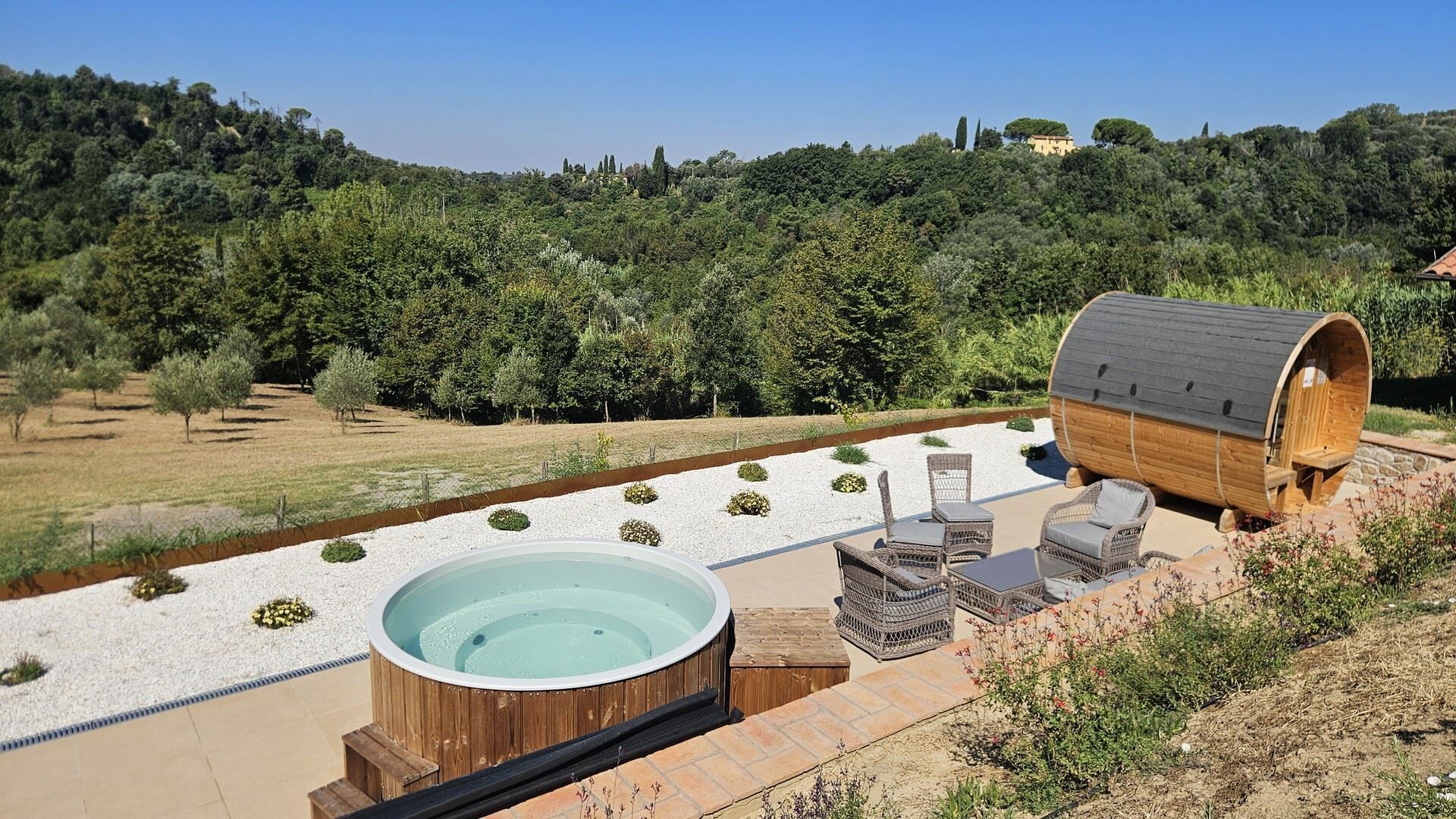 A hot tub with wicker furniture and a wooden barrel in a garden setting.