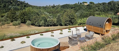 A hot tub with wicker furniture and a wooden barrel in a garden setting.